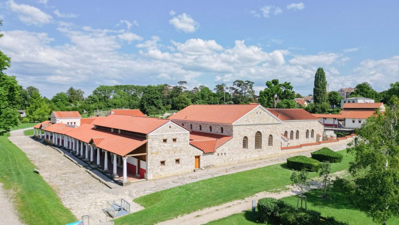 Römerstadt Carnuntum mit rekonstruierten Gebäuden und roten Dächern, umgeben von grünen Bäumen und Rasenflächen.