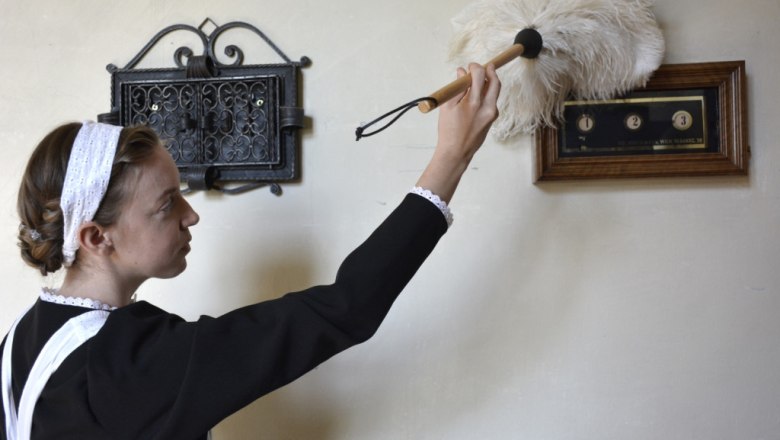 Eine Frau in historischer Kleidung staubt ein antikes Gerät ab.